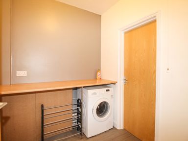 A laundry room with a washing machine under a wooden countertop a drying rack and a closed wooden door at The White Cottage in Weymouth
