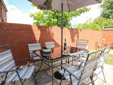 An outdoor patio with a glass table and six striped chairs under an umbrella at The White Cottage in Weymouth