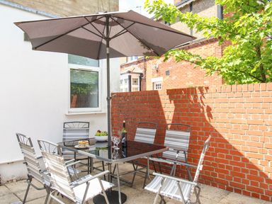 An outdoor patio area with a glass table six chairs and a large umbrella at The White Cottage in Weymouth