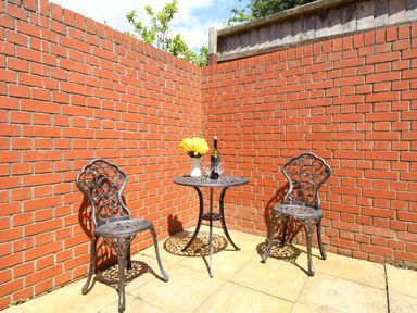 A small outdoor patio with a round metal table and two metal chairs against red brick walls at The White Cottage in Weymouth