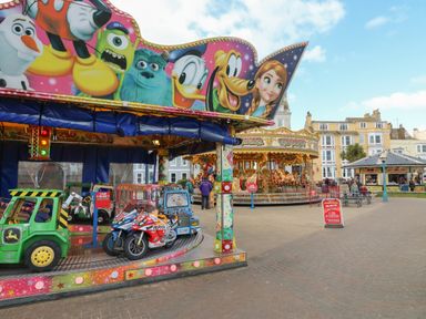 Children's amusement rides including a car and motorcycle carousel and a traditional horse carousel in a public square
