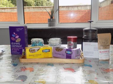 A kitchen table with cereals biscuits jars a coffee press and a coffee bag at The White Cottage in Weymouth
