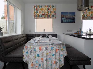 A dining area with a table set with plates and glasses surrounded by black cushioned bench seating at The White Cottage in Weymouth