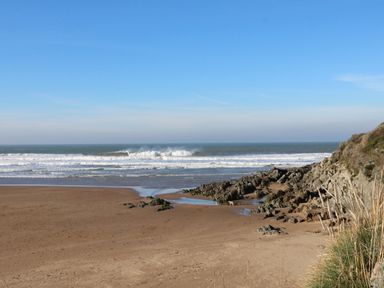 A beach with sand rocks and ocean waves under a clear blue sky at Old Maids Cottage in Woolacombe