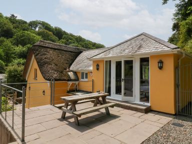 An outdoor area with a thatched roof and a garden table at Old Maids Cottage in Woolacombe