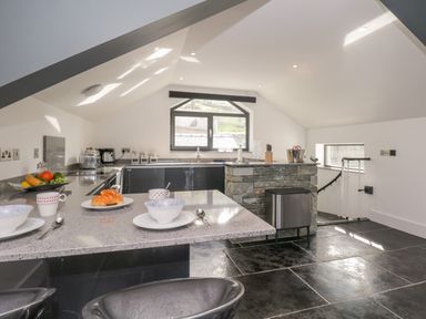A kitchen with a breakfast bar set with bowls and cups a stone island and a window at The Boat House at Louper Weir in Bowness-On-Windermere