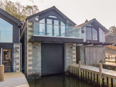 A waterfront property with stone walls and glass balconies over a dock at The Boat House at Louper Weir in Bowness-On-Windermere