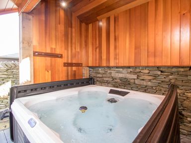 An indoor hot tub with wooden panel walls and a stone wall at The Boat House at Louper Weir in Bowness-On-Windermere