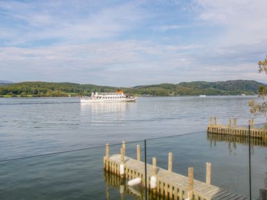 A lake with a boat and wooden docks surrounded by hills at The Boat House at Louper Weir in Bowness-On-Windermere