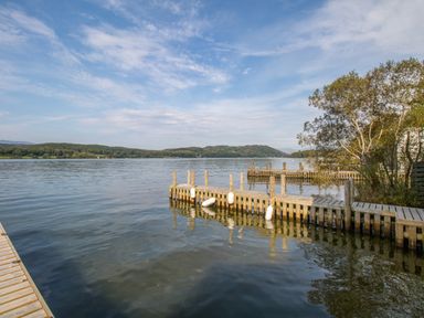 A wooden dock extending into a lake with hills and trees in the background at The Boat House at Louper Weir in Bowness-On-Windermere