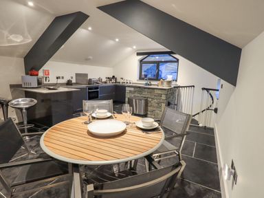 A kitchen and dining area with a round wooden table set for four and modern appliances at The Boat House at Louper Weir in Bowness-On-Windermere
