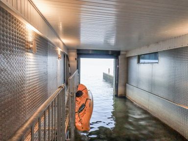 A boat storage room with an orange kayak partially in water and metal walls at The Boat House at Louper Weir in Bowness-On-Windermere