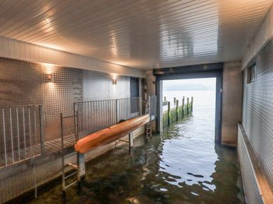 An indoor boat storage area with metal walls and ceiling a kayak on a rack and a view of a dock on water at The Boat House at Louper Weir in Bowness-On-Windermere