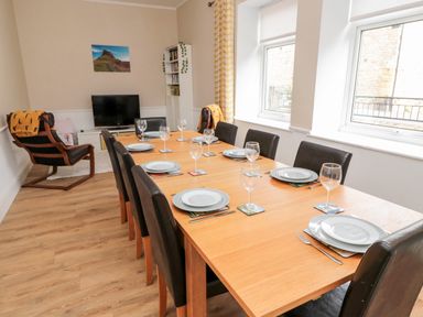 A dining room with a wooden table set for eight people and two windows at The Old Sweet Shop in Alnwick