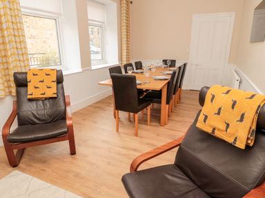 A dining room with a wooden table set for eight and two black leather chairs with yellow blankets at The Old Sweet Shop in Alnwick