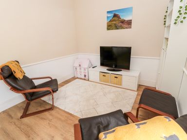 A sitting room with two chairs a television on a white cabinet and a toy dollhouse at The Old Sweet Shop in Alnwick