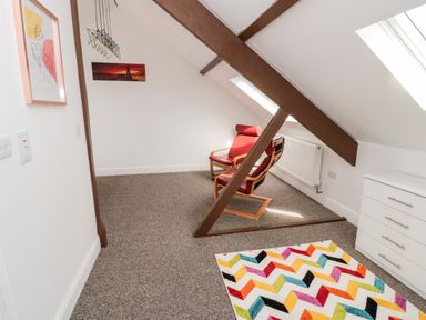 A room with two red chairs a colorful zigzag rug a white chest of drawers and framed artwork at The Old Sweet Shop in Alnwick