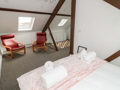 A bedroom with a bed, rolled towels, two red chairs, a dresser, and skylight windows at The Old Sweet Shop in Alnwick