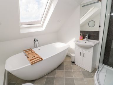 A bathroom with a freestanding bathtub under a skylight window a sink with a mirror and a corner shower at The Old Sweet Shop in Alnwick