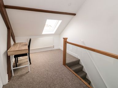 An attic room with a wooden desk a black chair a skylight window and stairs with a wooden handrail at The Old Sweet Shop in Alnwick