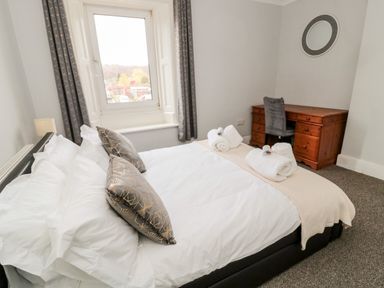 A bedroom with a bed and pillows beside a window and a wooden desk with a chair at The Old Sweet Shop in Alnwick