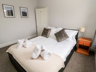 A bedroom with a bed with pillows and rolled towels bedside table lamp and pictures on the wall at The Old Sweet Shop in Alnwick