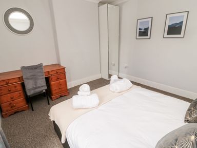 A bedroom with a bed and folded towels a wooden desk a chair a round wall mirror a full-length mirror and two framed pictures at The Old Sweet Shop in Alnwick