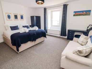 A bedroom with a double bed and sofa a wardrobe and desk near a window at The Old Sweet Shop in Alnwick