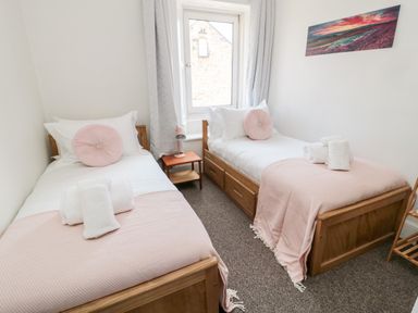 A bedroom with two single beds a small table with a lamp and a window at The Old Sweet Shop in Alnwick