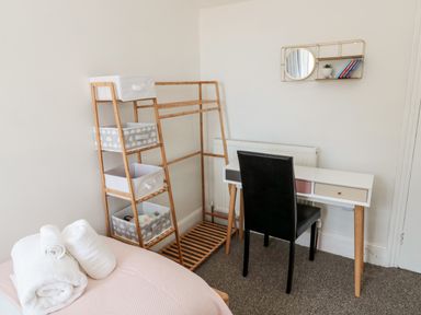 A bedroom corner with a small desk and chair next to a wooden clothes rack with storage bins at The Old Sweet Shop in Alnwick