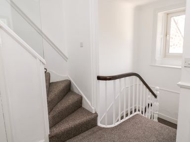 A carpeted staircase with white walls and a window at The Old Sweet Shop in Alnwick