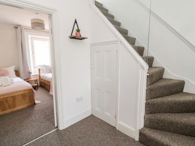 A hallway with carpeted stairs and a small door under the stairs next to a bedroom with two single beds at The Old Sweet Shop in Alnwick