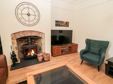 A living room with a fireplace wood stove a large clock above and a television on a wooden stand at The Old Sweet Shop in Alnwick