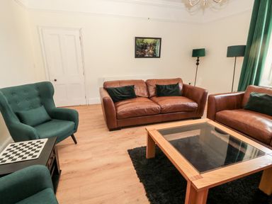 A living room with brown leather sofas green chairs a wooden coffee table and green curtains at The Old Sweet Shop in Alnwick