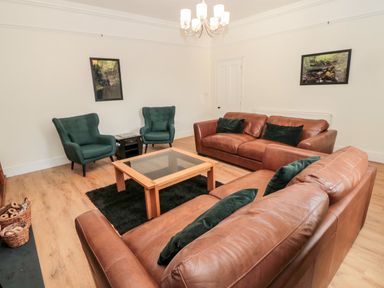A living room with two brown leather sofas two green armchairs a wooden coffee table and framed pictures on the walls at The Old Sweet Shop in Alnwick