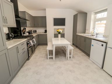 A kitchen with gray cabinets a white dining table with benches and a vase of flowers at The Old Sweet Shop in Alnwick