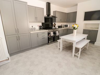 A kitchen with grey cabinets white table with bench and a vase of flowers on the table at The Old Sweet Shop in Alnwick