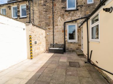 A small paved courtyard with a bench and storage box against a stone wall at The Old Sweet Shop in Alnwick