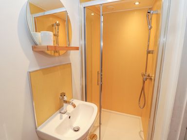 A bathroom with a sink a faucet a round mirror a wooden shelf with cups and a shower area at The Old Sweet Shop in Alnwick