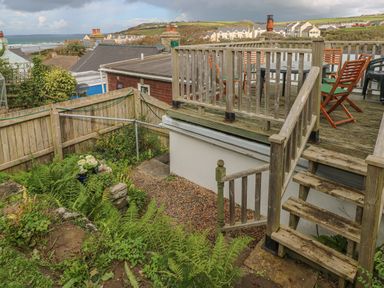 A wooden deck with chairs and table overlooking a garden with plants and a fence at Inglenook Cottage in Broad Haven