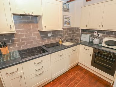 A kitchen with cream cabinets a black oven a microwave a kettle a sink and a tiled backsplash at Inglenook Cottage in Broad Haven