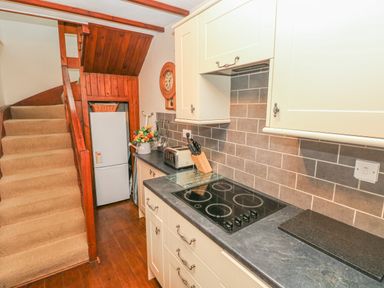 A kitchen with stovetop knives toaster refrigerator and stairs at Inglenook Cottage in Broad Haven