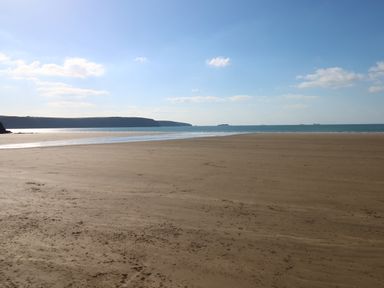 A sandy beach with calm sea and distant land under a blue sky at Inglenook Cottage in Broad Haven