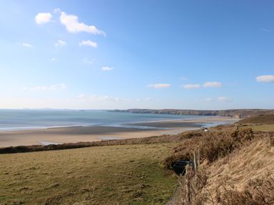 A coastal landscape with a sandy beach water cliffs and grassy fields at Inglenook Cottage in Broad Haven