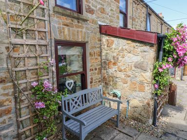 A stone cottage exterior with a wooden bench and flowering climbing plants on trellises at Inglenook Cottage Broad Haven