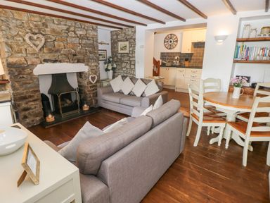 A living room with stone fireplace grey sofas a wooden dining table and kitchen area at Inglenook Cottage in Broad Haven