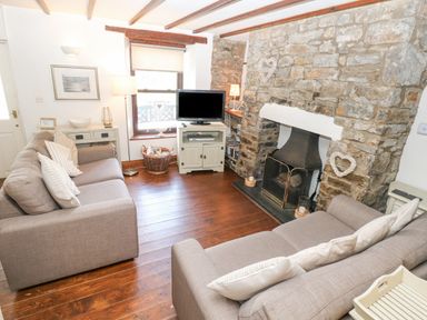 A living room with two gray sofas a stone fireplace a television on a cabinet and wooden flooring at Inglenook Cottage Broad Haven
