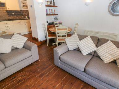 A living area with two sofas with striped cushions a small round dining table with chairs and a kitchen with white cabinets at Inglenook Cottage in Broad Haven