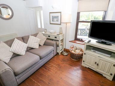A living room with a gray sofa and striped pillows a floor lamp a TV on a cabinet and a basket on a wooden floor at Inglenook Cottage in Broad Haven