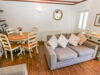 A living room with a gray sofa with striped pillows a wooden dining table with four chairs and a vase with flowers at Inglenook Cottage in Broad Haven